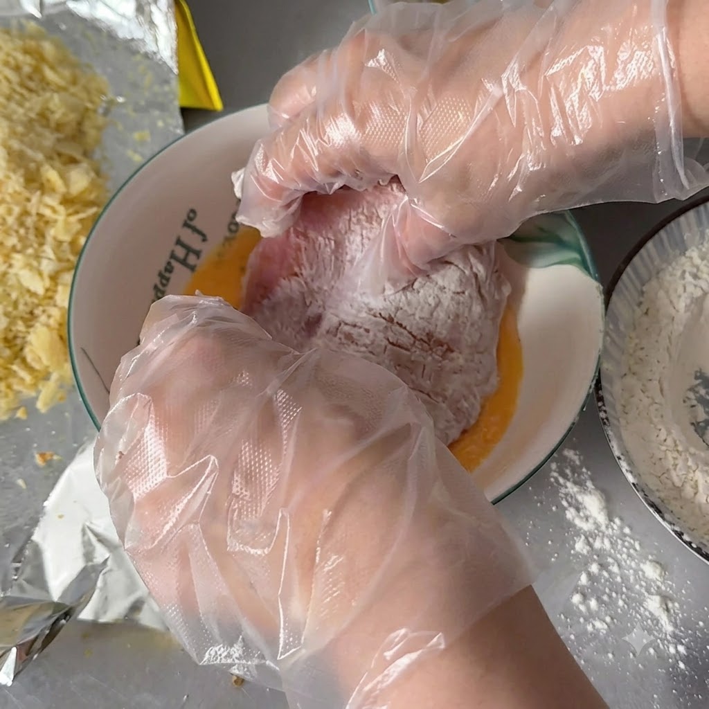 Manos con guantes sumergiendo una chuleta empolvada de harina en un bol con huevos batidos dorados.