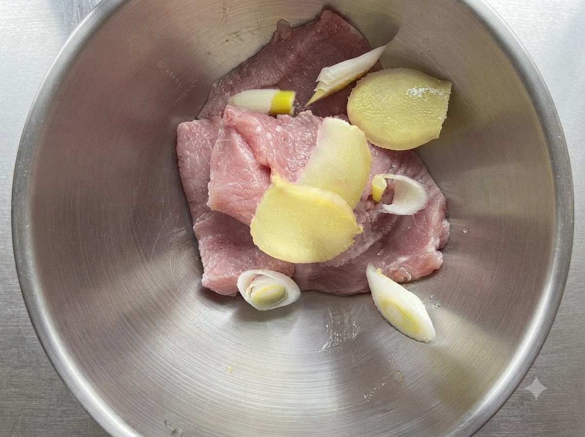 Rodajas de lomo de cerdo en un bol metálico mezcladas con cebollín y rodajas de jengibre.