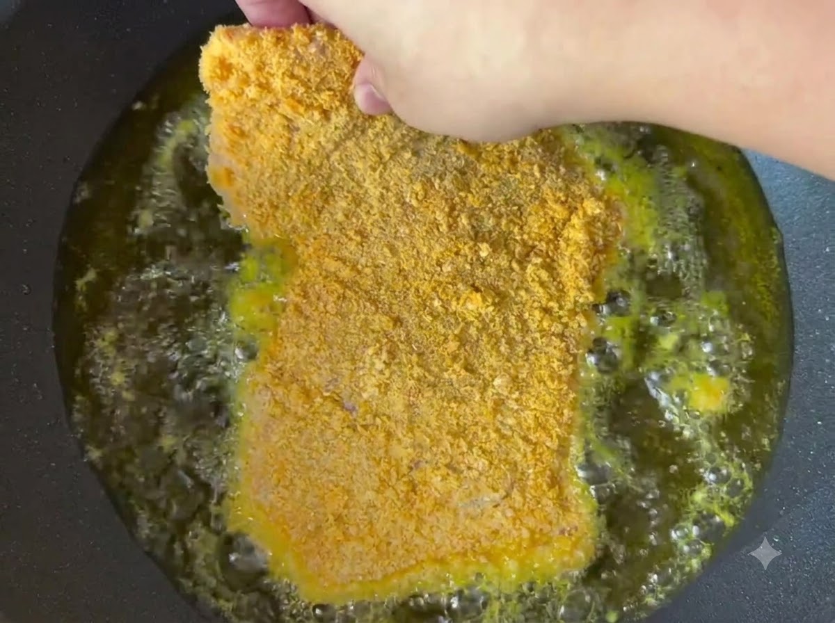 Una chuleta de cerdo empanada friéndose en aceite caliente dentro de una sartén.
