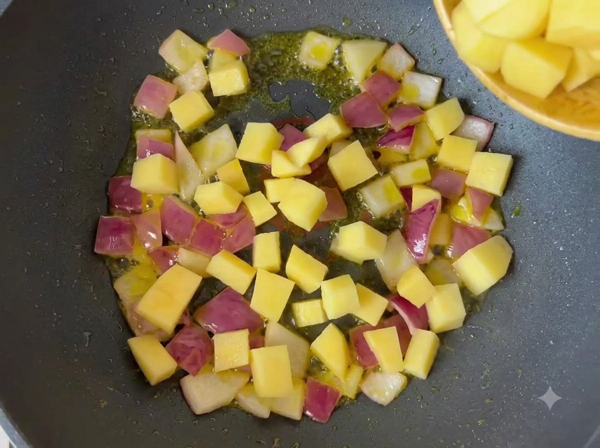 Patatas amarillas picadas y cebollas mezclándose en una sartén con aceite.