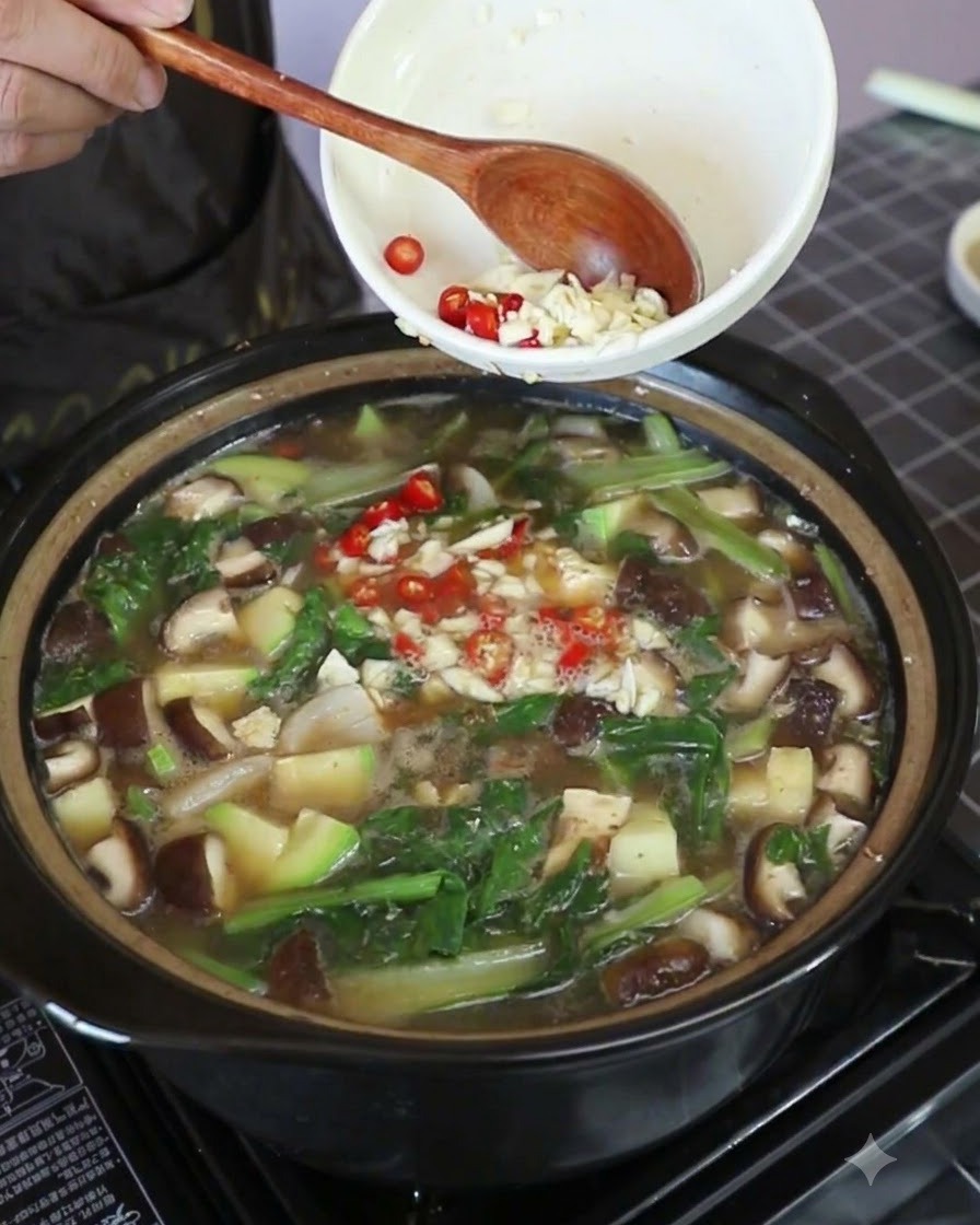 Ajo picado y trozos de chile tailandés rojo brillante siendo incorporados al estofado hirviendo.