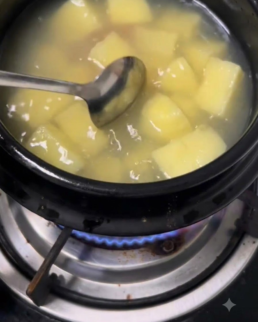 Una cuchara removiendo pasta de soja y pasta de ají en una olla con agua y patatas.
