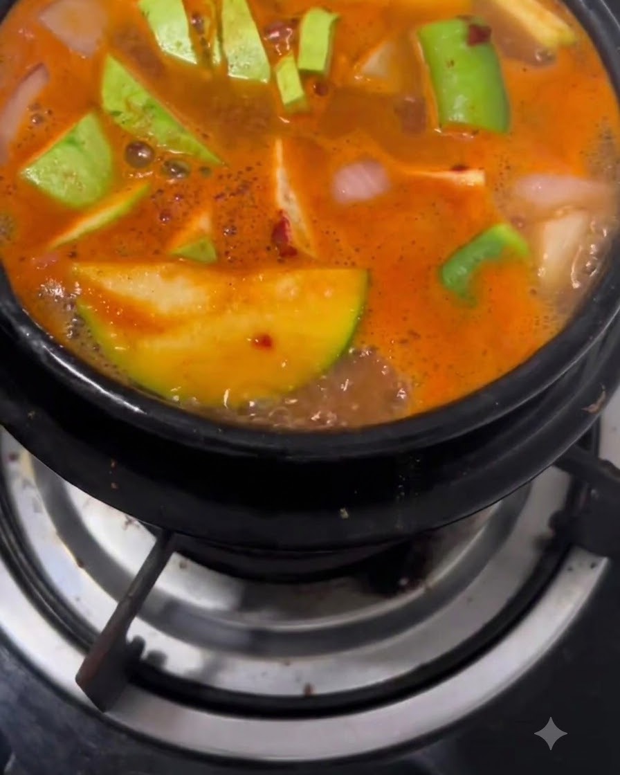 Una olla de barro llena de doenjang jigae burbujeante hirviendo a fuego lento en un quemador de estufa de gas.
