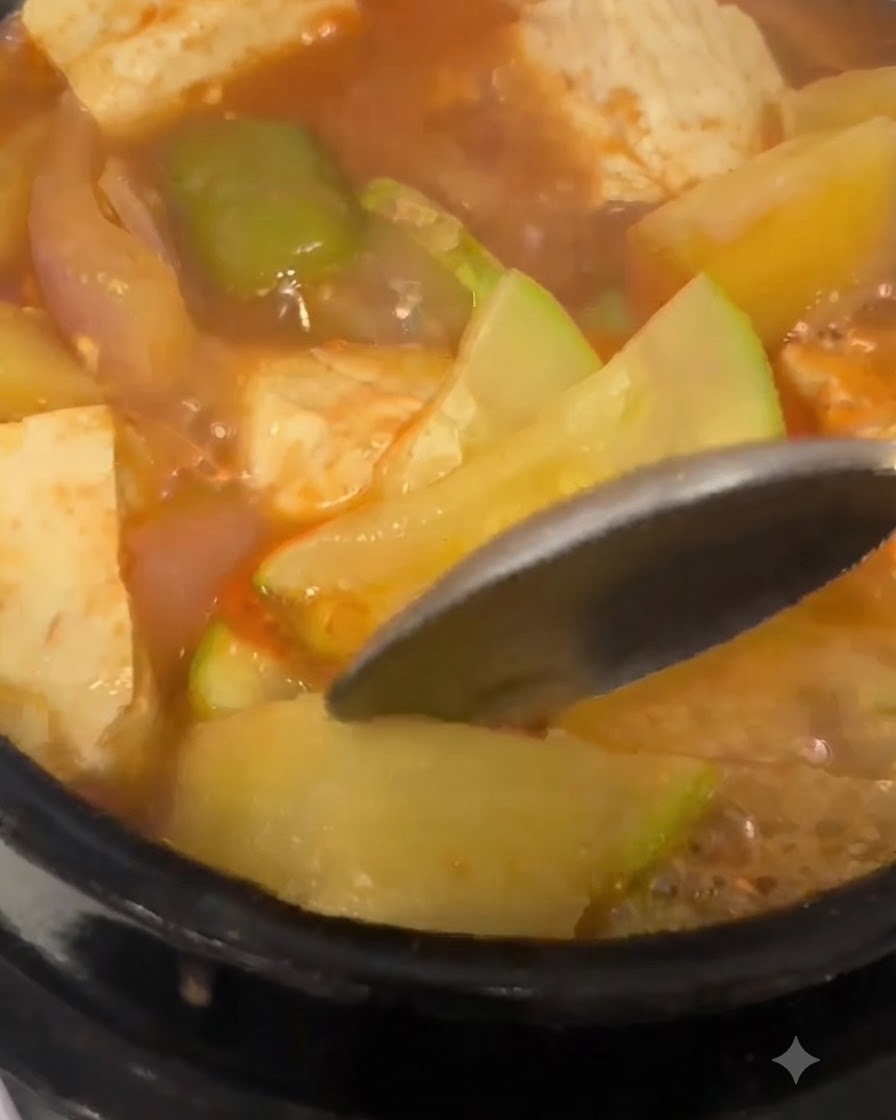 Una cuchara presionando contra una rodaja de patata tierna dentro del guiso coreano hirviendo de pasta de soja.
