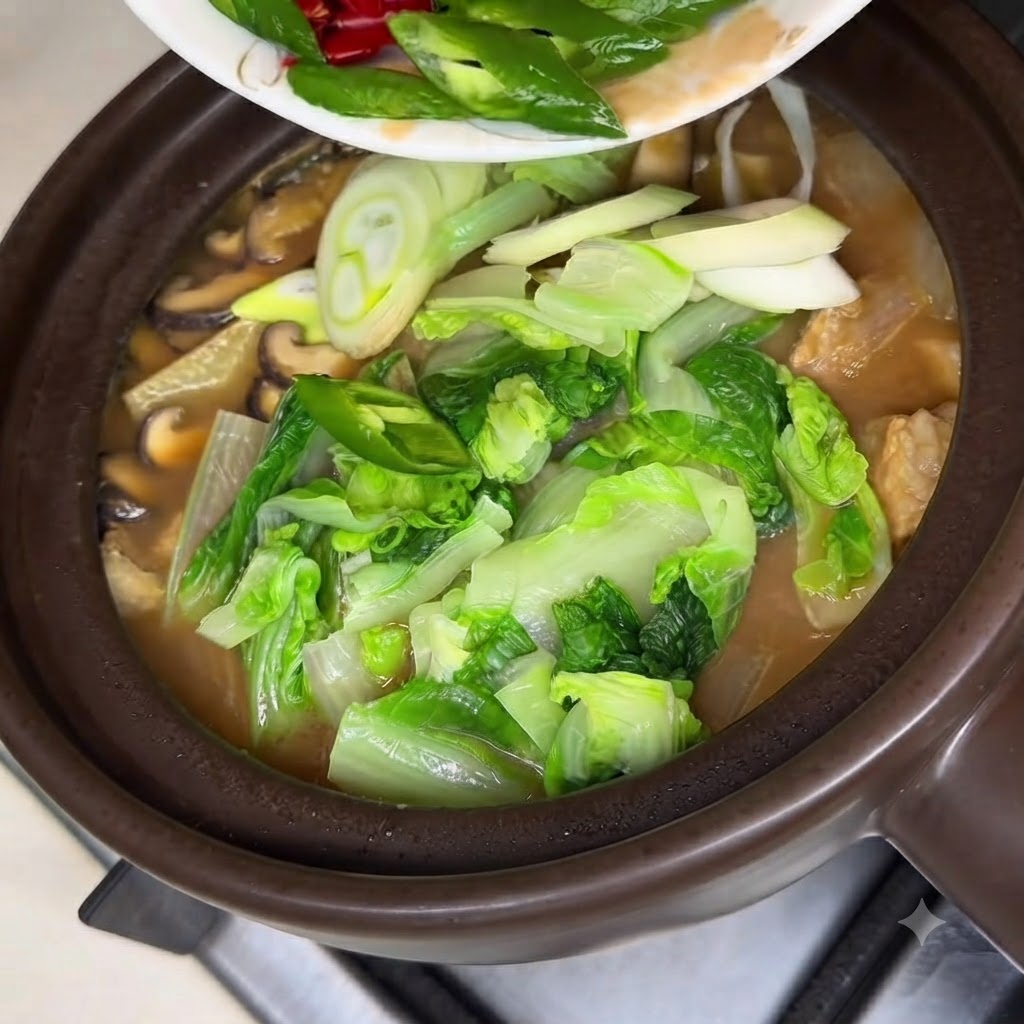 Saborizante de carne en polvo siendo espolvoreado desde una cuchara de madera en una cazuela de barro llena de estofado coreano de pasta de soja burbujeante.