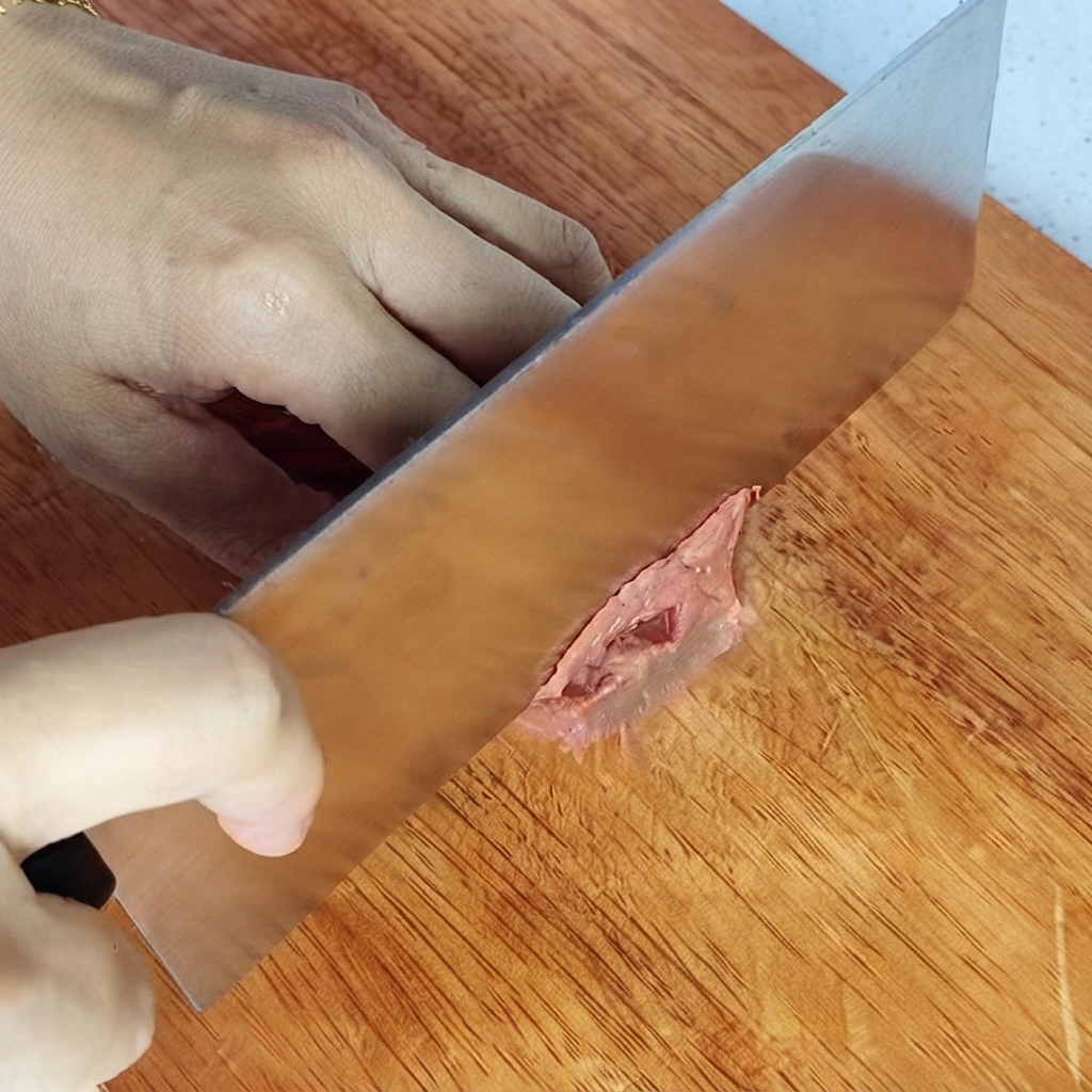Manos sosteniendo un cuchillo picando un trozo de lomo de res en una tabla de cortar de madera.