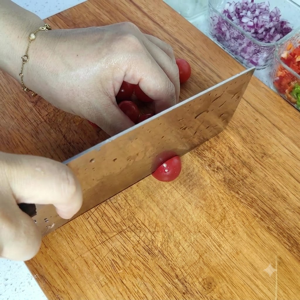 Cortando tomates cherry de color rojo brillante por la mitad en una tabla de cortar de madera.