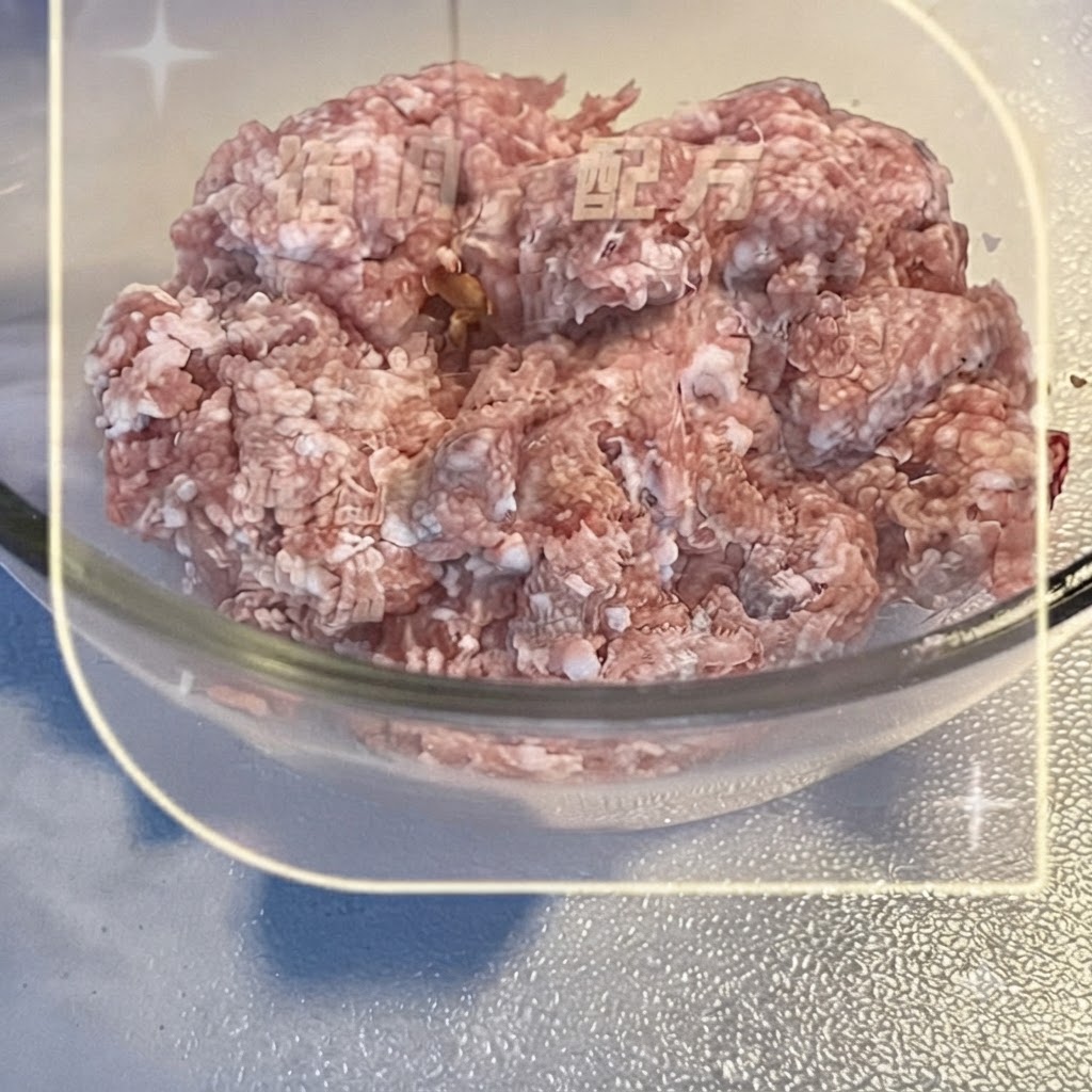 Carne de cerdo picada dentro de un tazón de vidrio transparente siendo mezclada con condimentos líquidos.