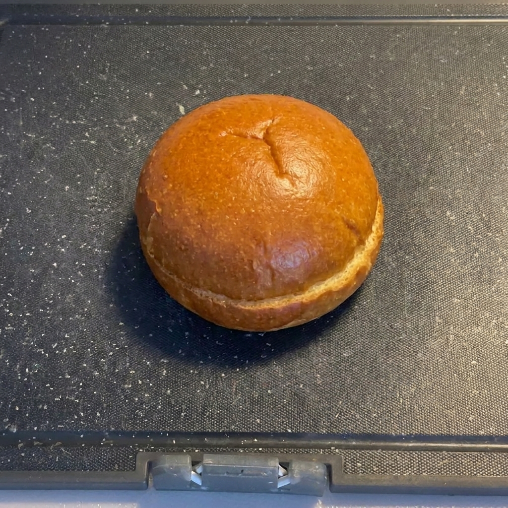 Mitades de pan de hamburguesa colocadas sobre una superficie de tabla de cortar oscura.