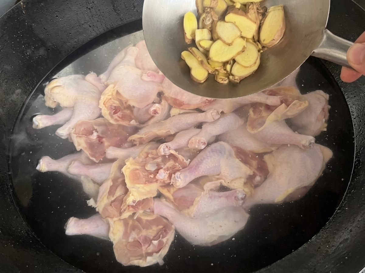 Añadiendo jengibre en rodajas en un wok que contiene trozos de pollo y agua.