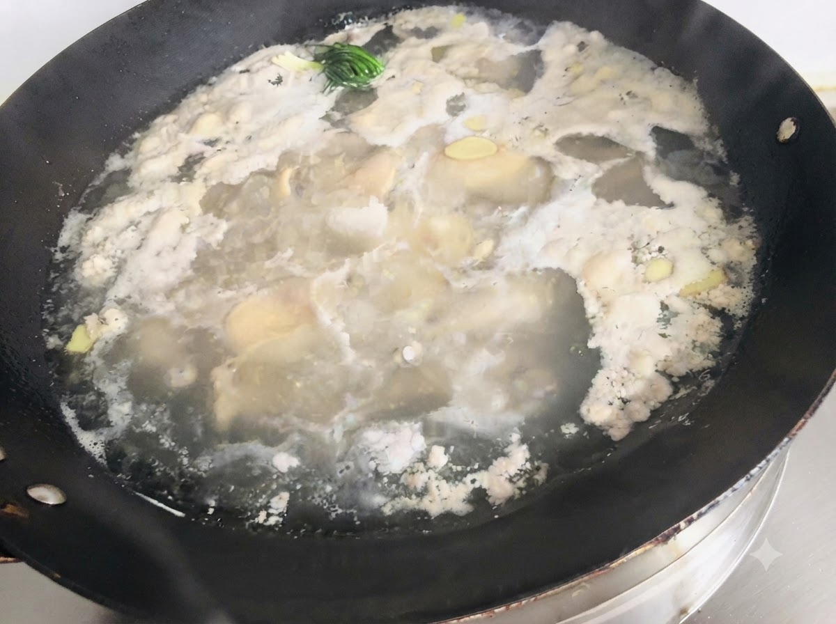 Espuma y residuos flotando sobre el agua hirviendo y los aromáticos en un wok grande.