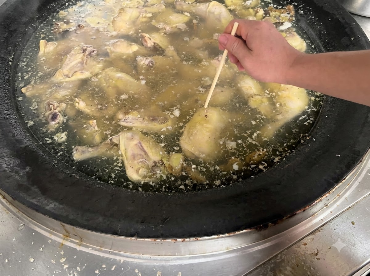 Una mano usando un palillo de madera para perforar un trozo de pollo que se cocina en una olla grande de caldo.