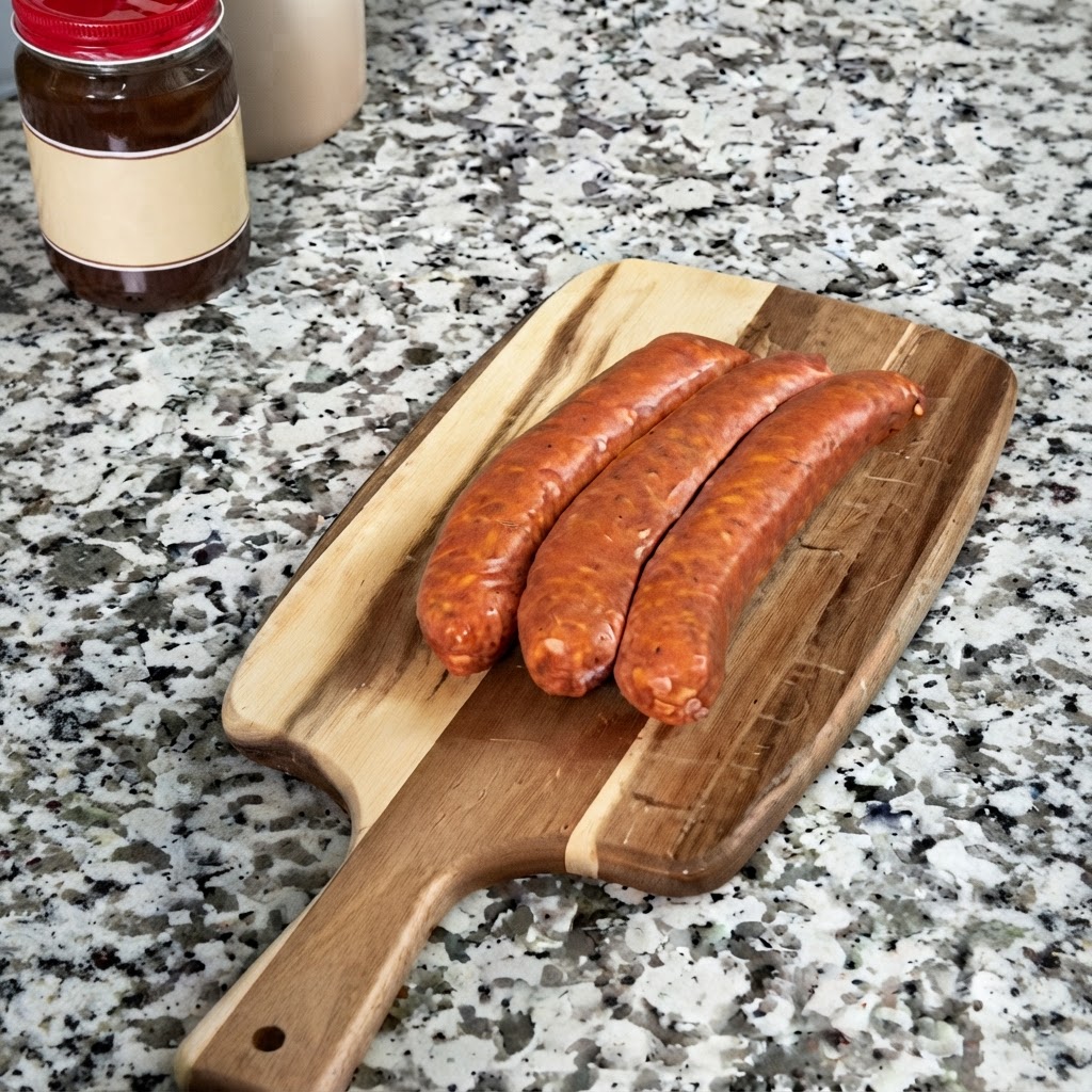Rodajas de salchicha andouille dispuestas en una tabla de cortar de madera junto a un frasco de roux.