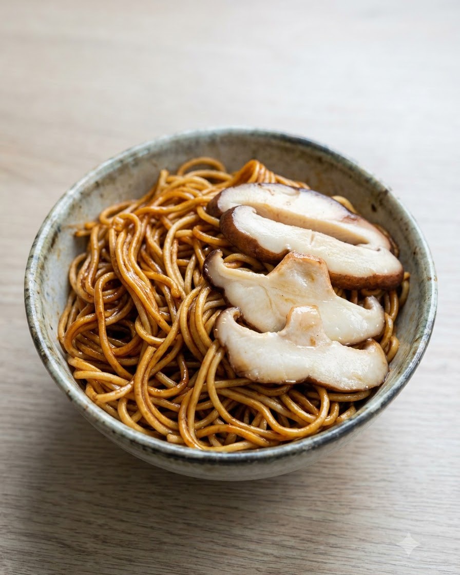 Rodajas de champiñones shiitake cocidos dispuestas ordenadamente sobre un tazón de fideos oscuros mixtos.