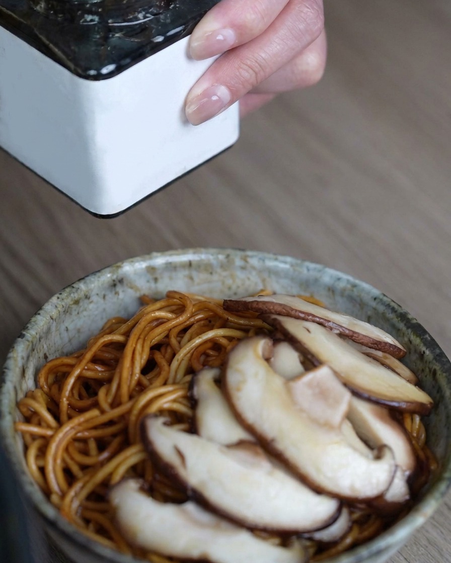 Una cucharada de pasta de trufa negra cayendo sobre los fideos cubiertos de champiñones.