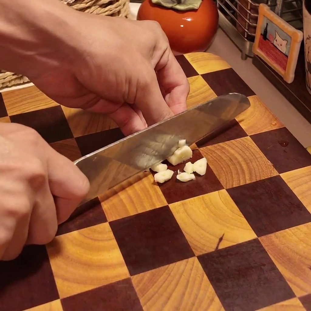 Una persona picando dientes de ajo en trozos pequeños sobre una tabla de cortar de madera a cuadros.