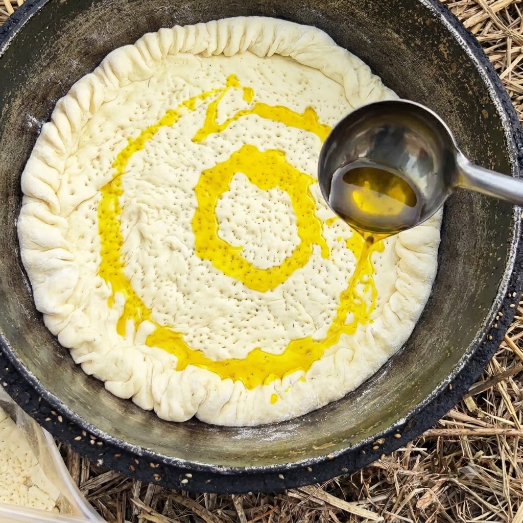 Un cucharón de metal vertiendo aceite de cocina amarillo sobre la masa dentro de una olla.