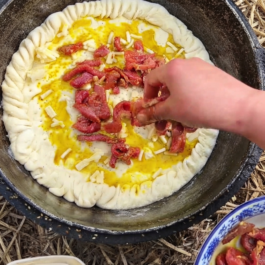 Una mano colocando tiras de ternera sazonada rojiza sobre una base de masa cubierta de queso en una sartén.