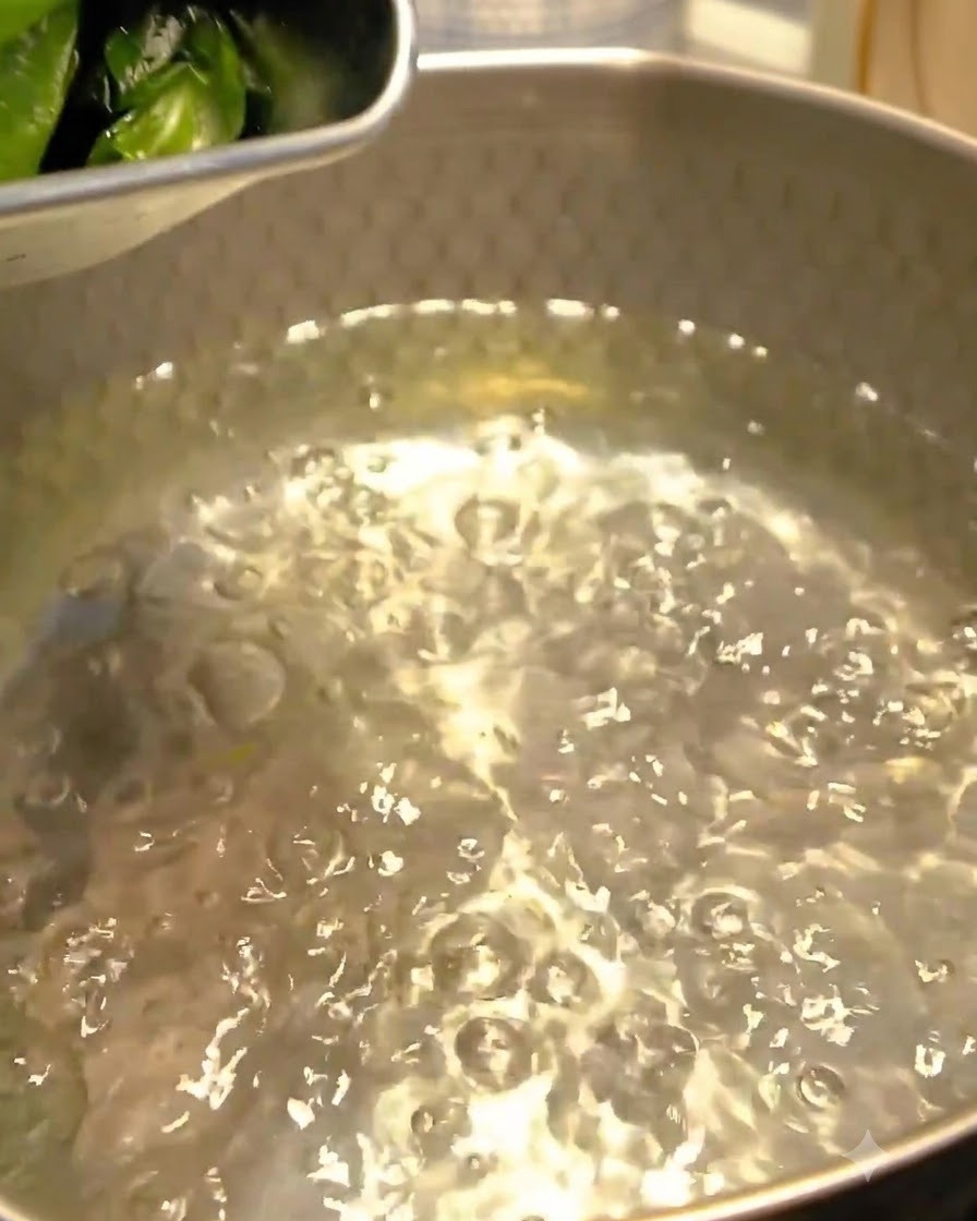 Alga wakame siendo añadida al agua hirviendo en una olla de metal.