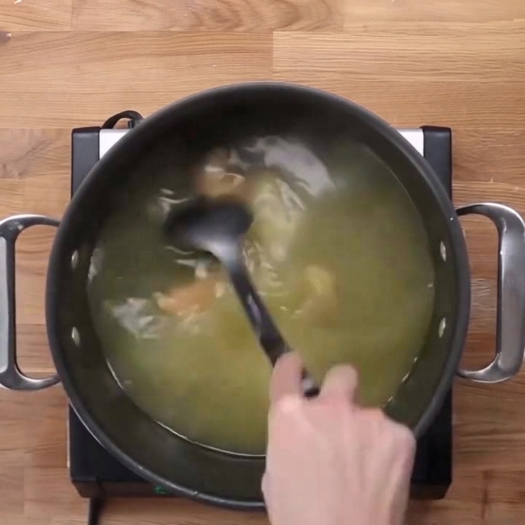 Caldo de sopa de miso siendo removido en una olla grande con un cucharón negro.
