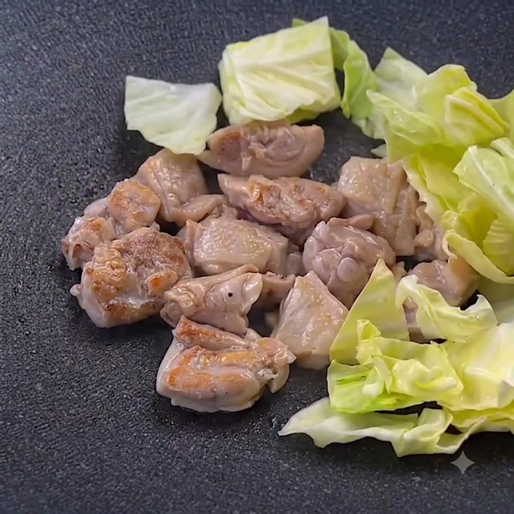 Hojas de repollo verde picadas colocadas junto al pollo frito en una sartén.
