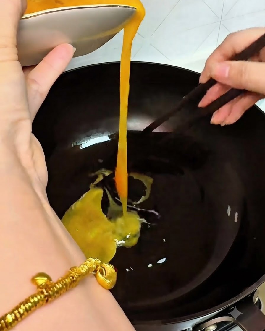 Huevos batidos amarillos vertiéndose en un wok caliente desde un tazón blanco mientras se revuelven con palillos.